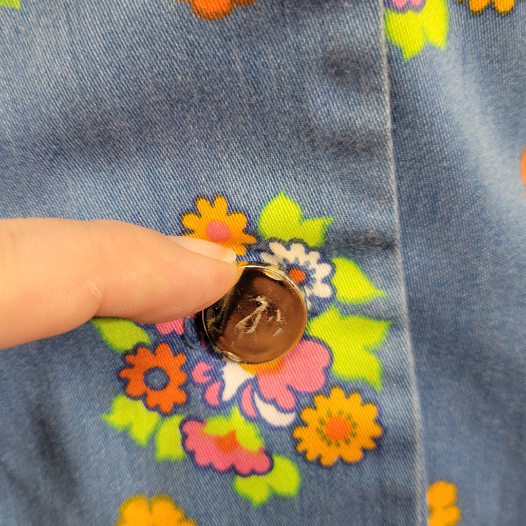 Close-up of a button on floral denim fabric with a hand pressing it.