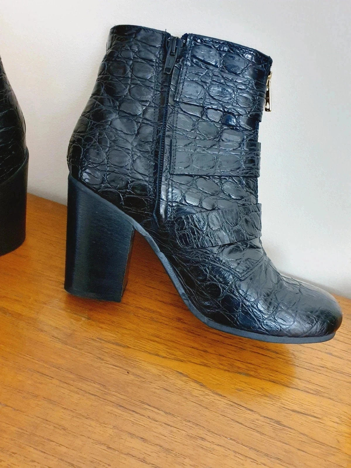 Black crocodile-patterned boot on a wooden surface with a white background