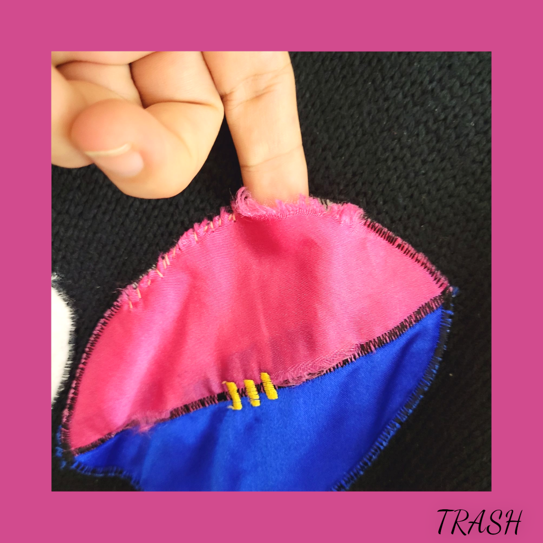 Hand holding a small pink and blue fabric item with yellow buttons on a black background.