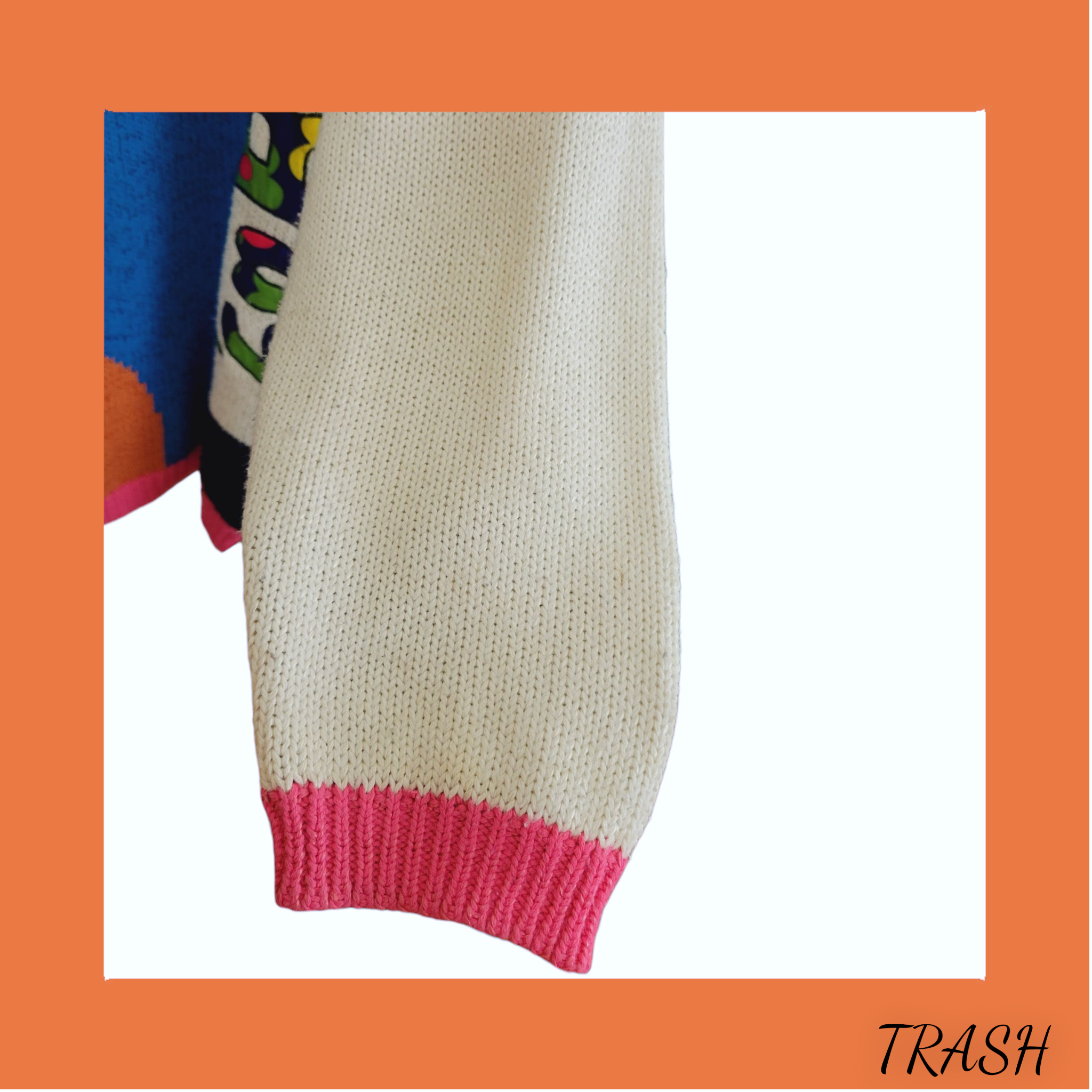 Close-up of a knitted sleeve with colorful cuffs and hem on an orange background, labeled 'TRASH'.