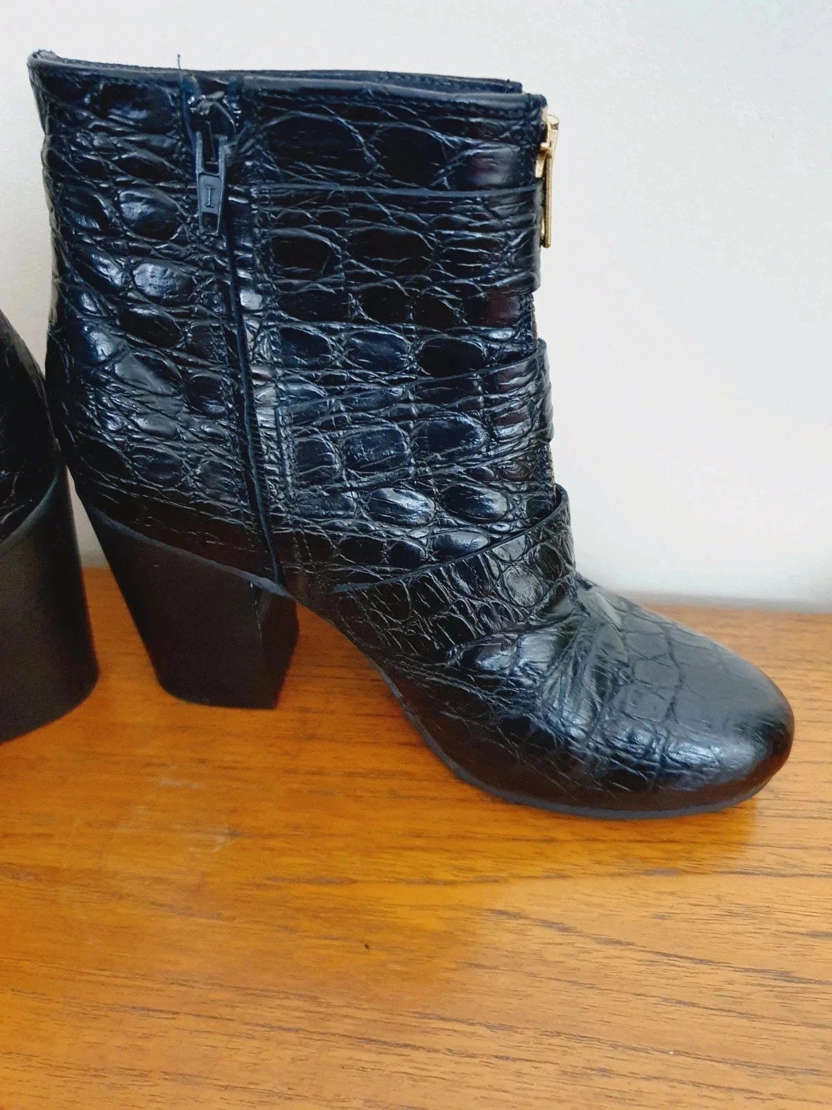 Black crocodile-patterned boots on a wooden surface with a white background